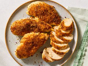 Overhead shot of a plate with three seasoned whole chicken breasts an one sliced chicken breast