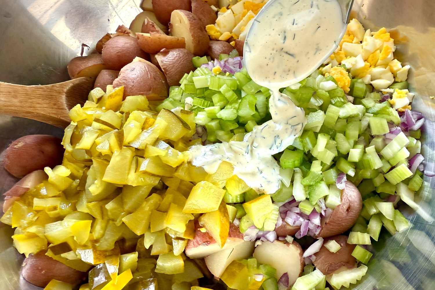 Ingredients for a potato salad being prepared, celery, pickles, potatoes, and a creamy dressing