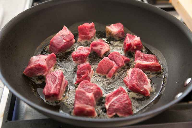 Several Beef Chunks being cooked to a brown in frying pan