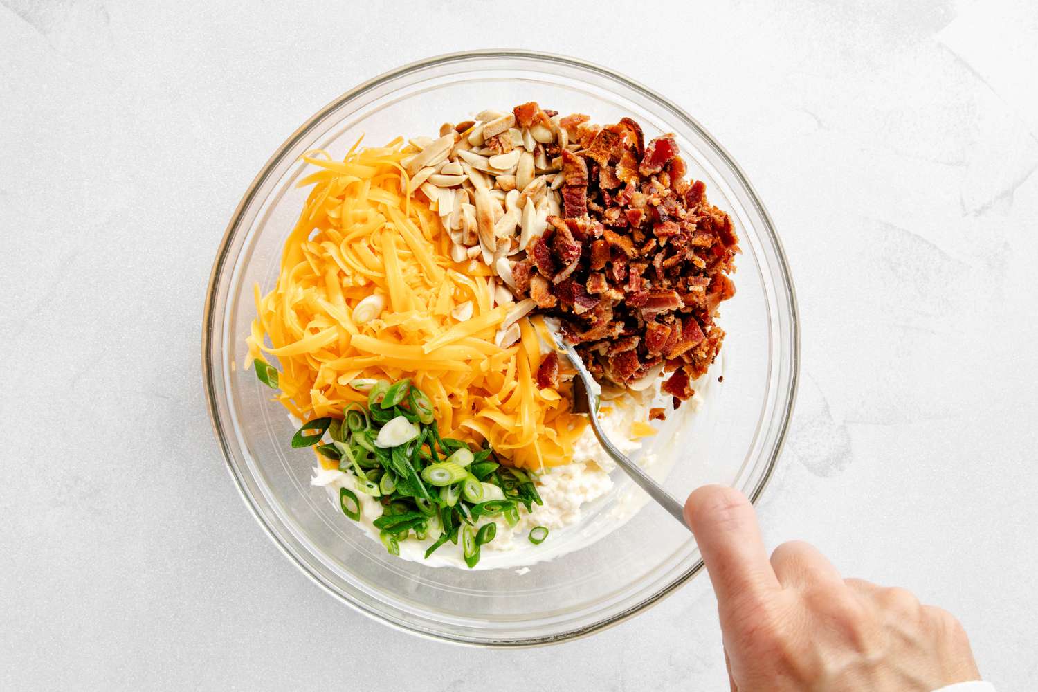 Shredded cheese, scallions, almonds, and bacon pieces added to bowl with cream cheese and mayo mixture for million dollar chicken recipe