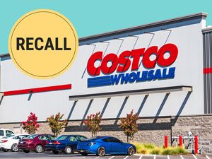 Costco storefront with a recall announcement badge above it parked cars in the foreground
