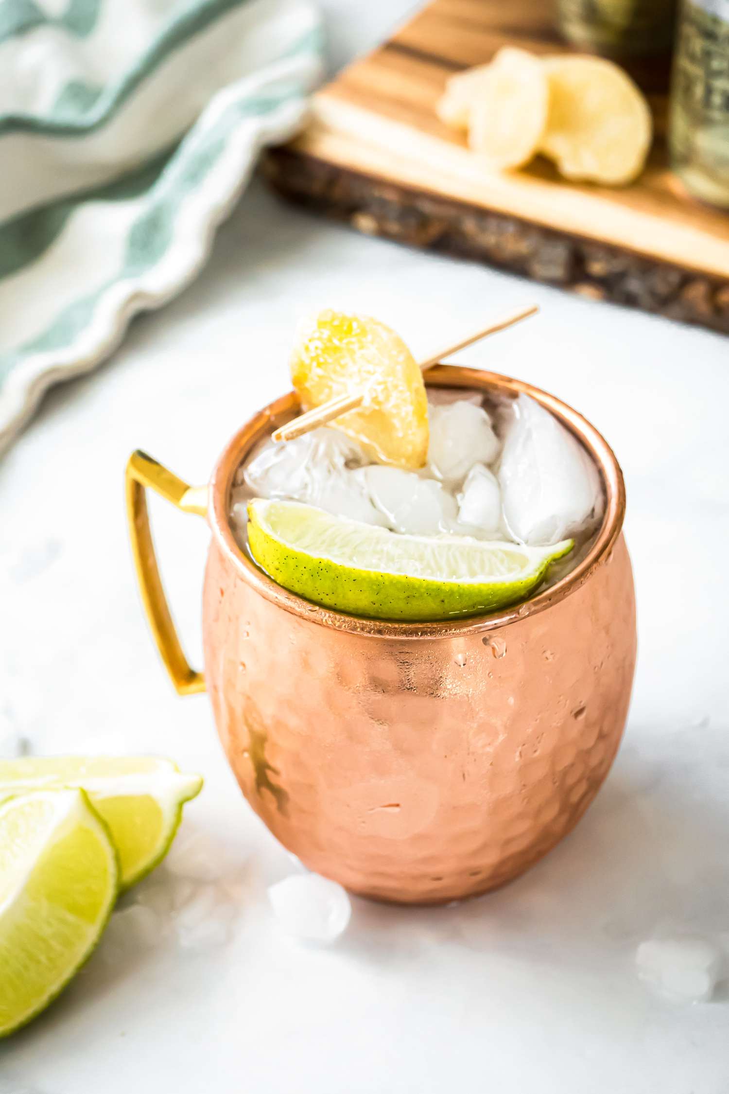 Mezcal Mule in Copper Mug with Lime and Candied Ginger, Surrounded by Lime and Ice 