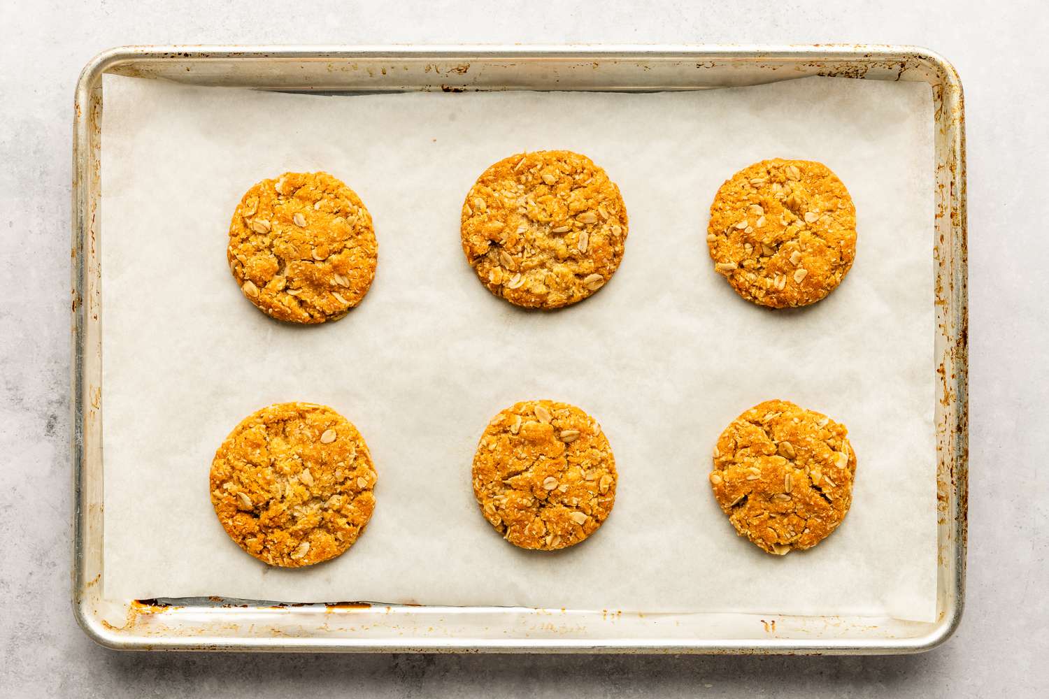 Six cookies for the Anzac Biscuits recipe baked on a parchment paper lined baking sheet