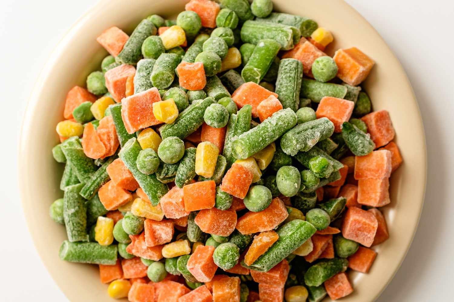 A bowl of mixed frozen vegetables including carrots green beans peas and corn