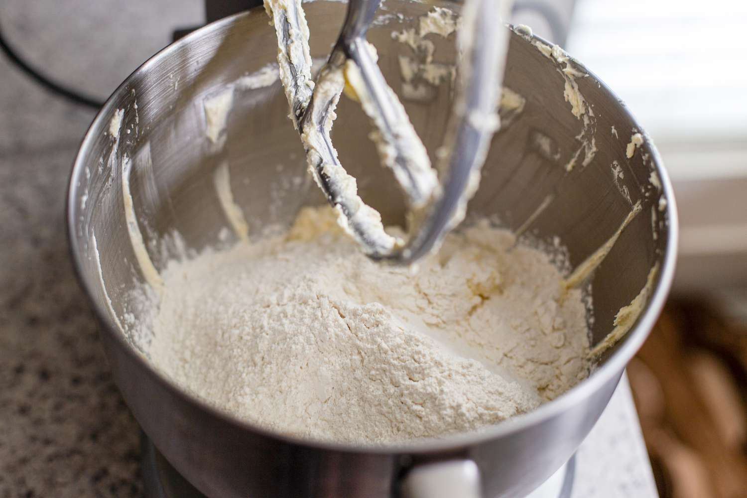 Adding dry ingredients to the bowl to make marzipan stamped cookies.