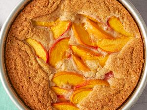 Baked peach spoon cake in a round pan featuring peach slices in a golden uneven cake top