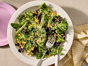 A plate of corn and black bean salad with leafy greens, garnished and served with utensils