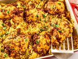 Baked chicken thighs on seasoned rice in a rectangular baking dish with a serving spatula