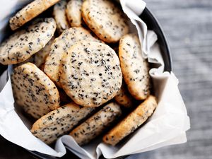 Buttery sesame cookies in a cookie tin lined with white tissue paper. 