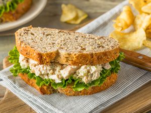 chicken salad and chips on a table napkin over a wooden board 