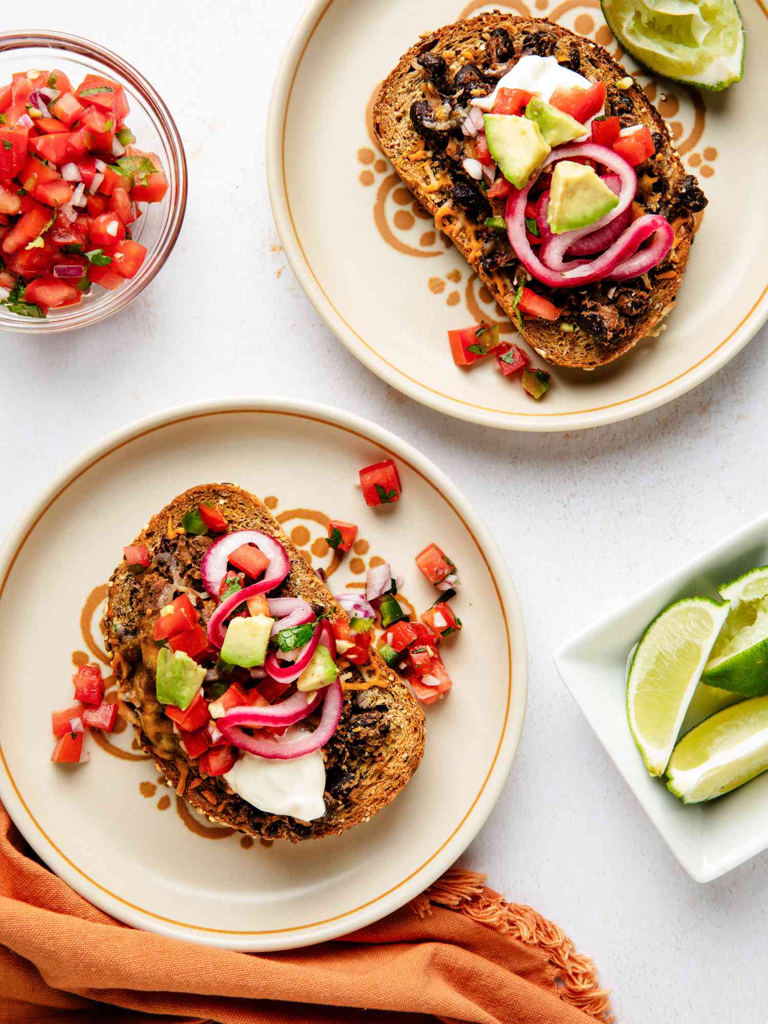 Two plates each with a black bean toast on top with lots of toppings