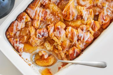 A baked apple cinnamon cobbler with icing in a white casserole pan a serving spoon scooping a portion from one end