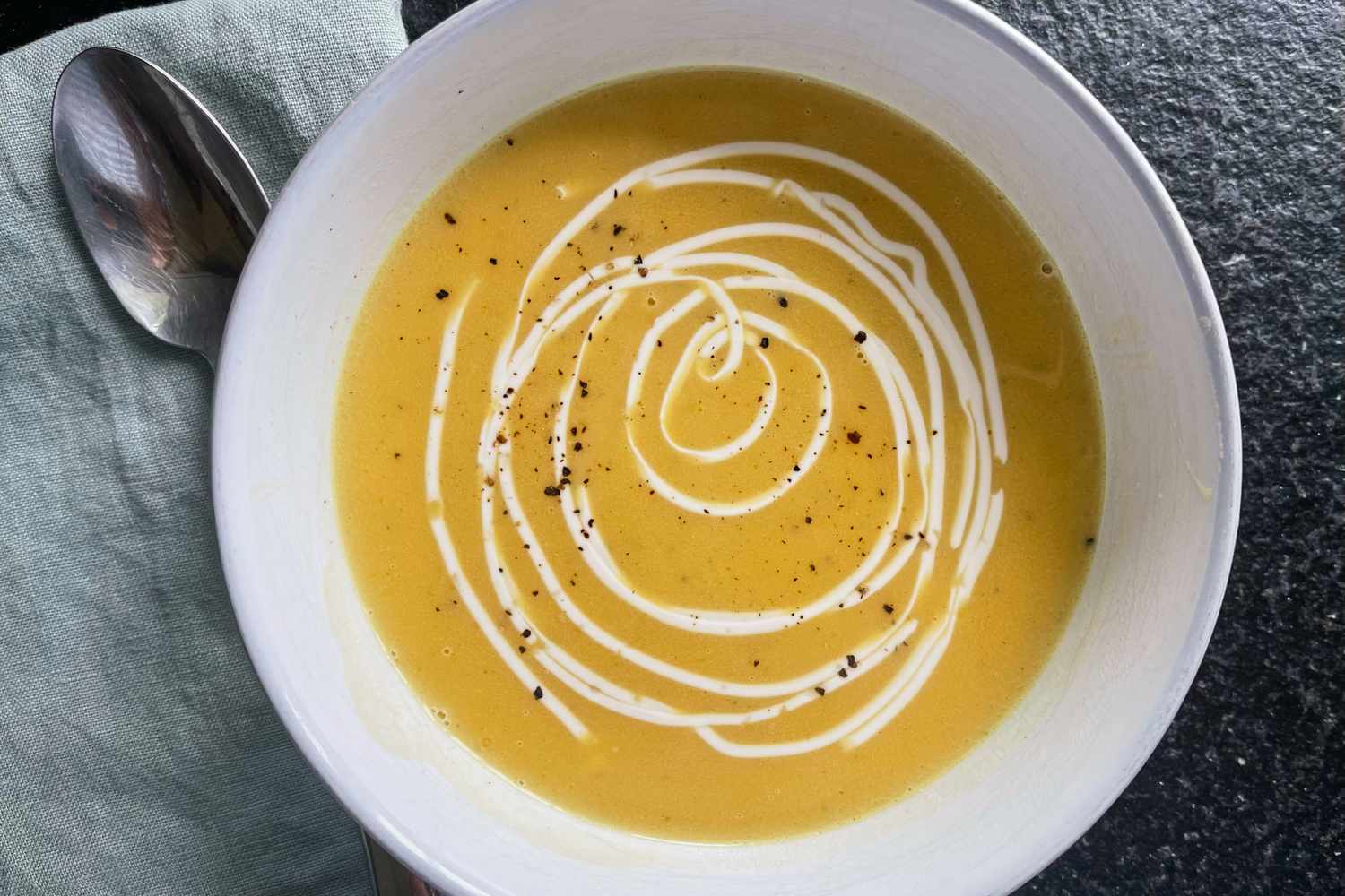 A bowl of butternut squash soup with a swirl of cream and cracked black pepper on top