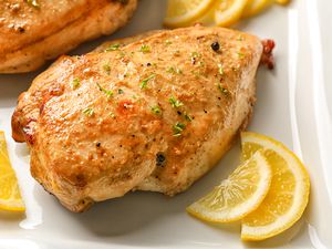 Closeup view of a roasted chicken breast with lemon slices on a white plate