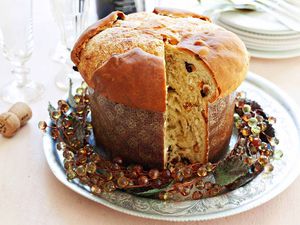 A loaf of homemade panettone in a paper mold with a slice cut out with a wreath around the base.