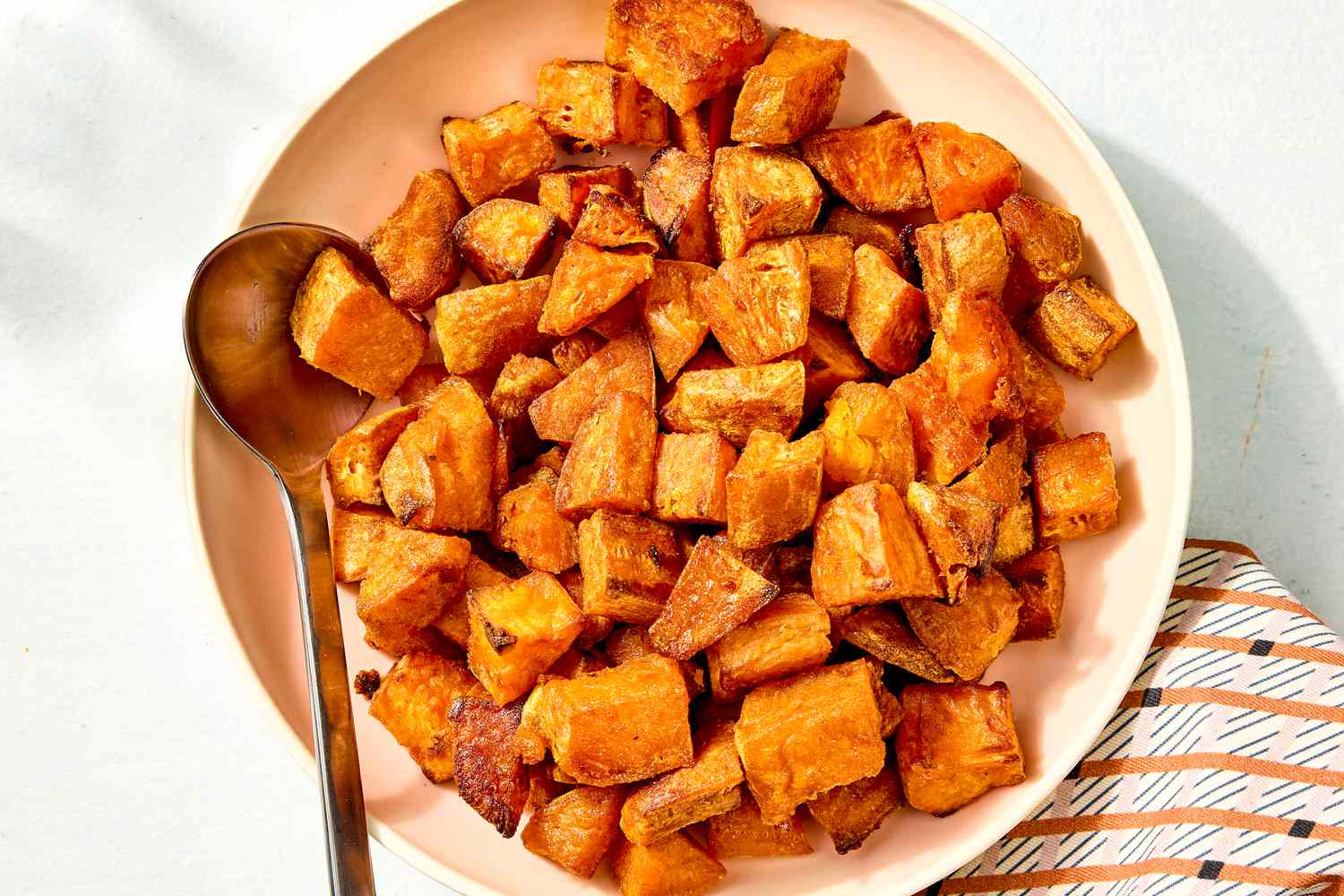 Overhead view of a bowl with cubes of roasted sweet potato along with a metal spoon