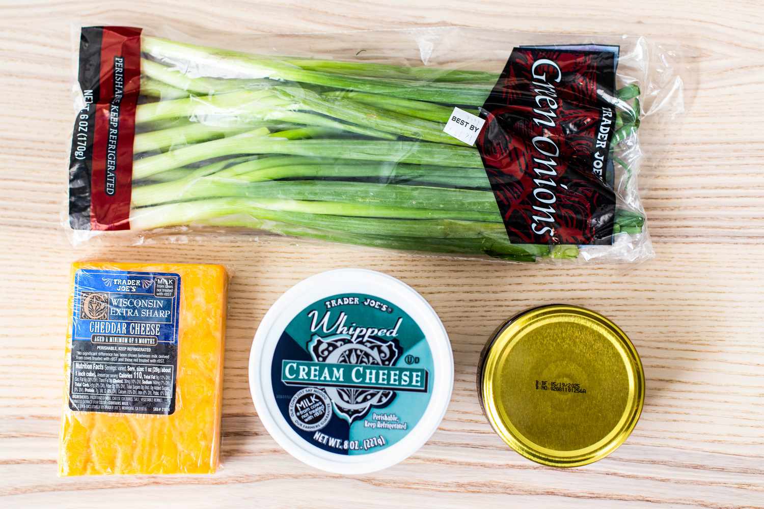 Chutney cheese appetizer ingredients on the counter. Top to bottom: pacakage of green onions, a block of cheddar cheese, whipped cream cheese, and a jar of chutney 