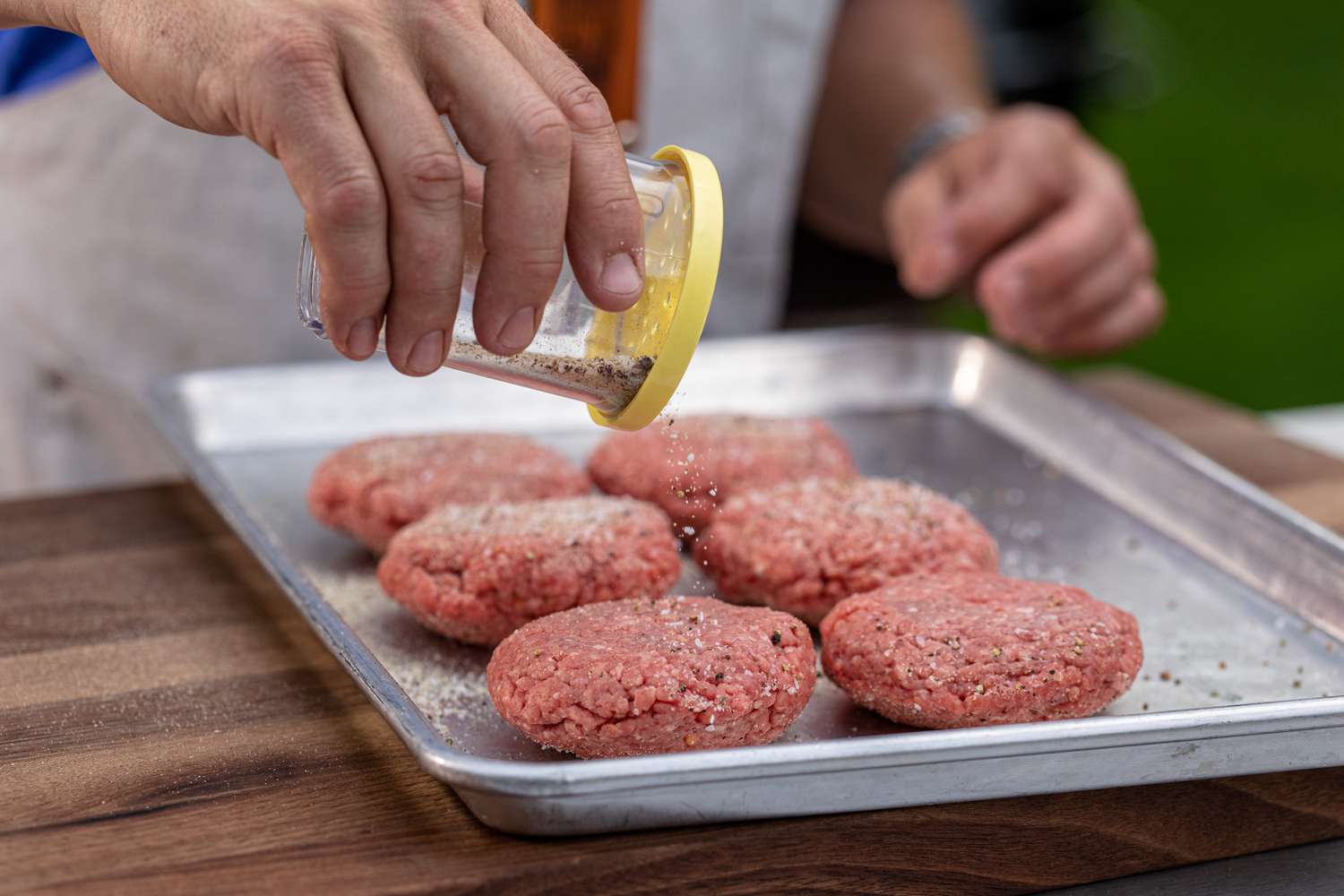 Adding seasoning to hamburger patties to make the best bacon cheeseburger.