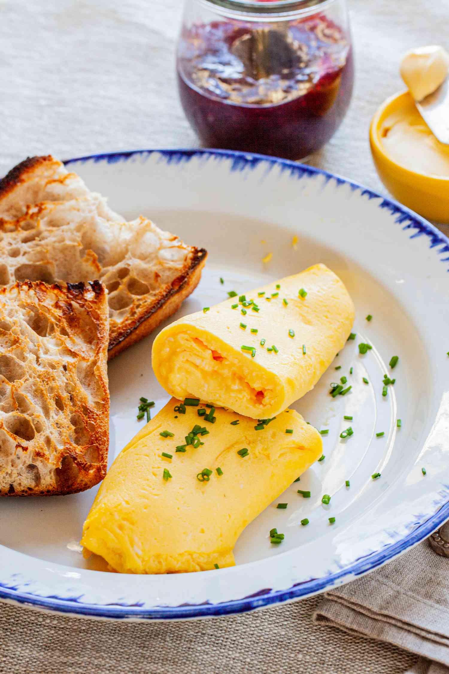 French Omelette Cut in Half and Bread on Plate with Jam and Butter in Background