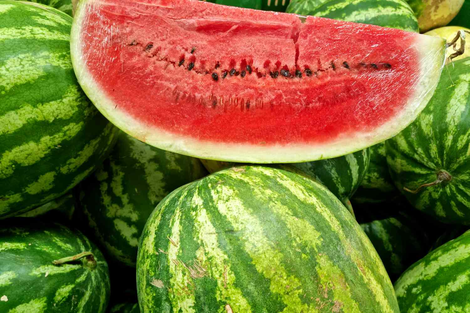 A cut piece of watermelon displayed on whole watermelons