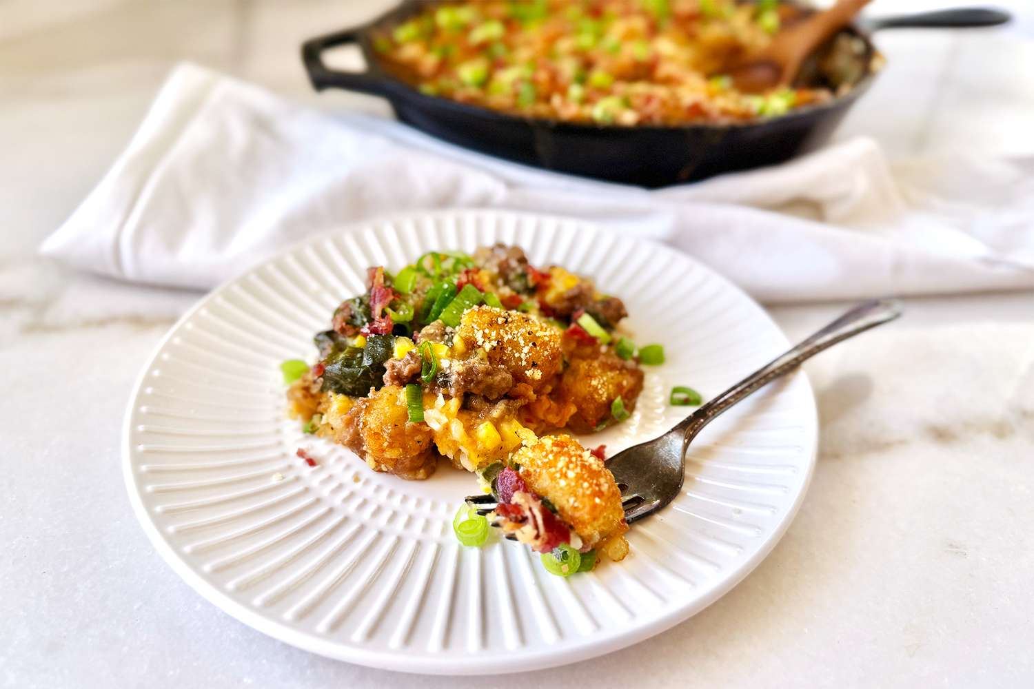 A plate of casserole served with a fork with additional casserole visible in a skillet in the background