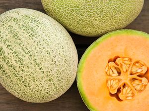 Whole cantaloupes and a cantaloupe half exposing seeds, placed on a textured surface