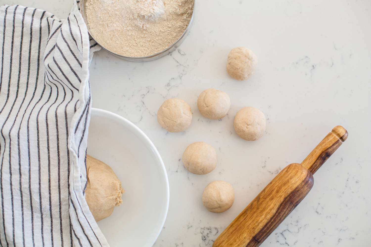 Small dough balls, a rolling pin, and flour to show how to make roti.