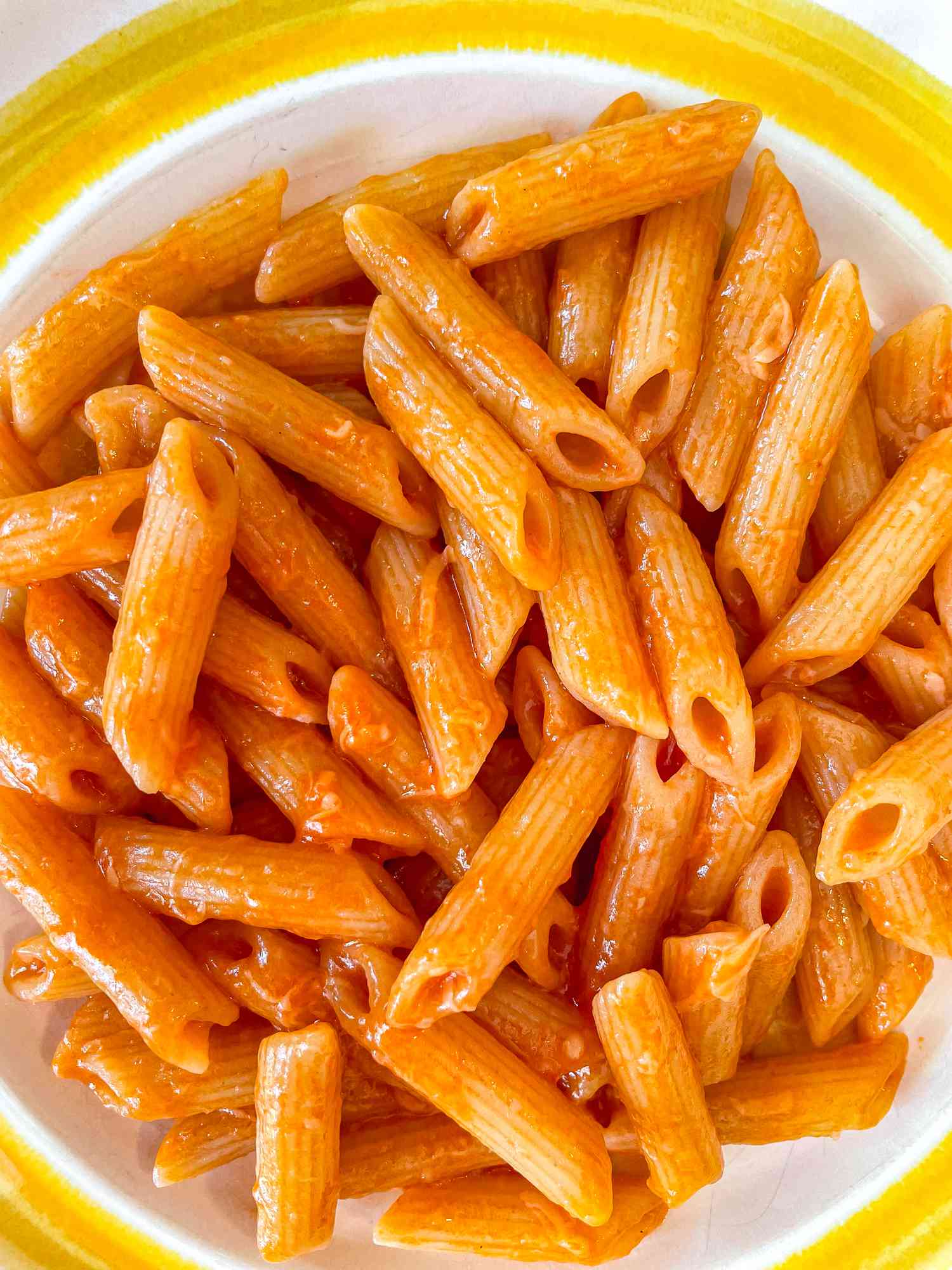A close up of tomato sauce-slicked penne in a wide, shallow bowl