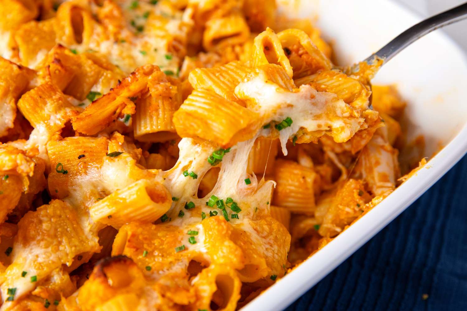 Baked pasta dish with chicken pumpkin and cheese in a casserole dish being served with a fork