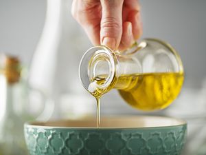 Pouring olive oil from a small bottle into a ceramic bowl