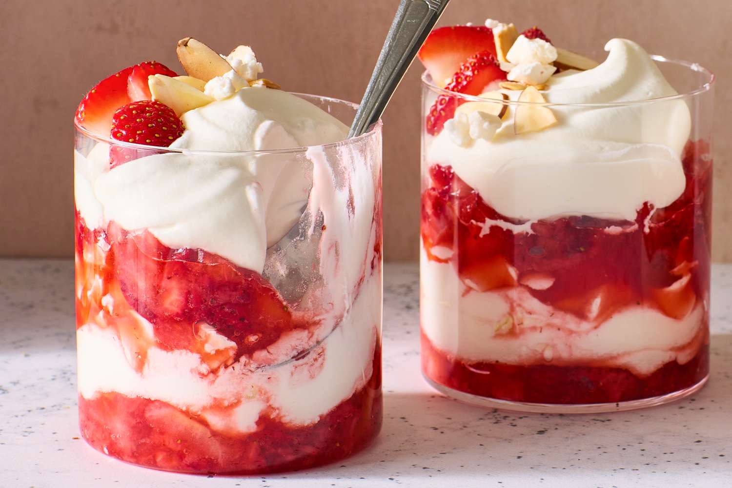 Two glasses of strawberry Eton Mess with whipped cream and strawberries, dessert served on a speckled surface