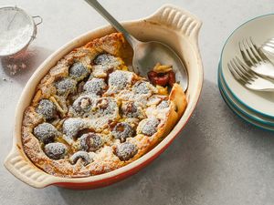 Cherry clafoutis served in a baking dish with a serving spoon, plates and forks are set nearby