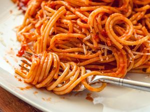 pasta (in marinara sauce) wrapped around a fork on a plate with more sauced pasta