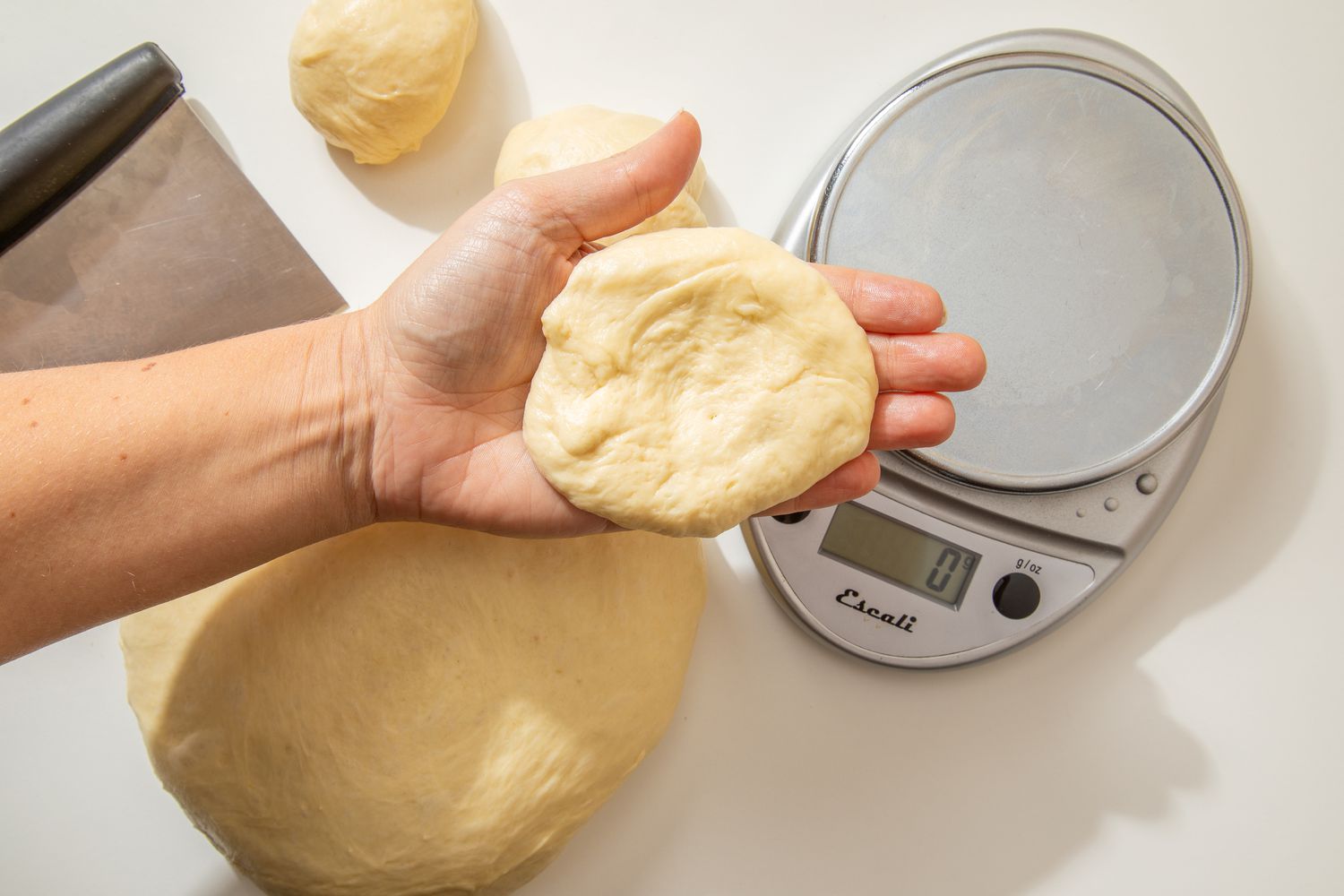 Shaping the roll: hand holding a flattened dough ball for salted honey rolls recipe