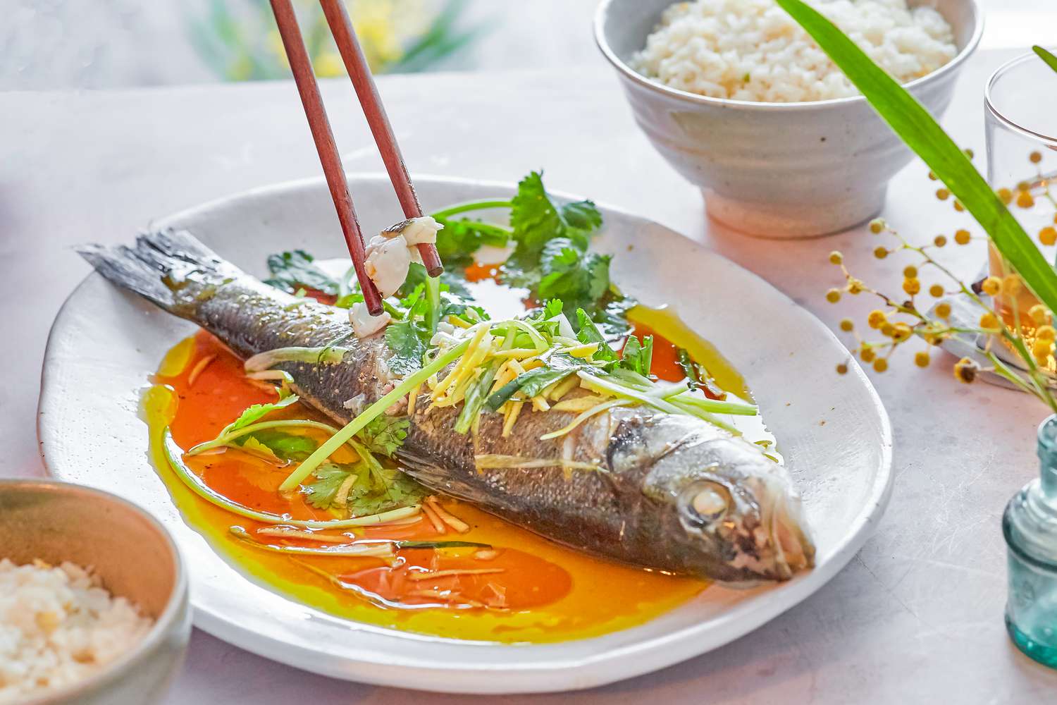 Chopsticks picking up a bite of steamed whole fish off a platter.
