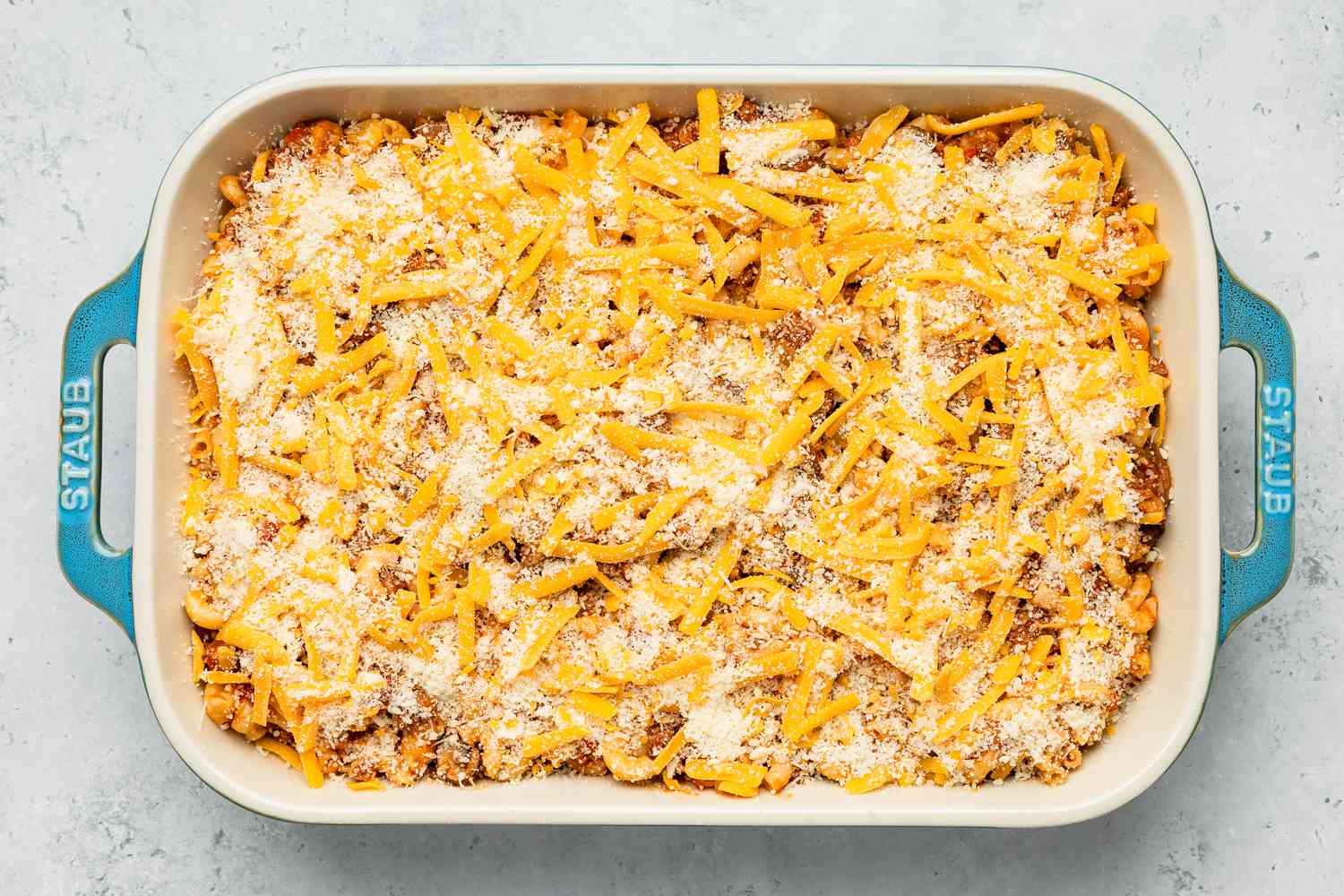 Casserole dish with Johnny Marzetti casserole ingredients topped with grated cheddar and parmesan cheese
