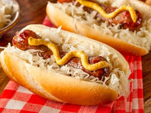 Two bratwurst sausages served in buns topped with mustard and sauerkraut on a checkered tablecloth