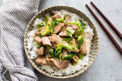 Pork stir-fry with green onions served on rice in a bowl, chopsticks on the side