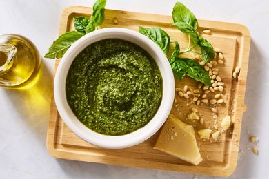 Bowl of basil pesto surrounded by basil leaves pine nuts cheese and olive oil