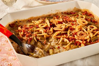 Angled view of a beige casserole dish with green bean casserole along with a serving spoon