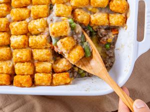 hand with wooden spoon scooping out some Classic Tater Tot Hotdish out of baking dish
