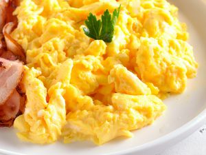 scrambled eggs on a plate with slices of bacon