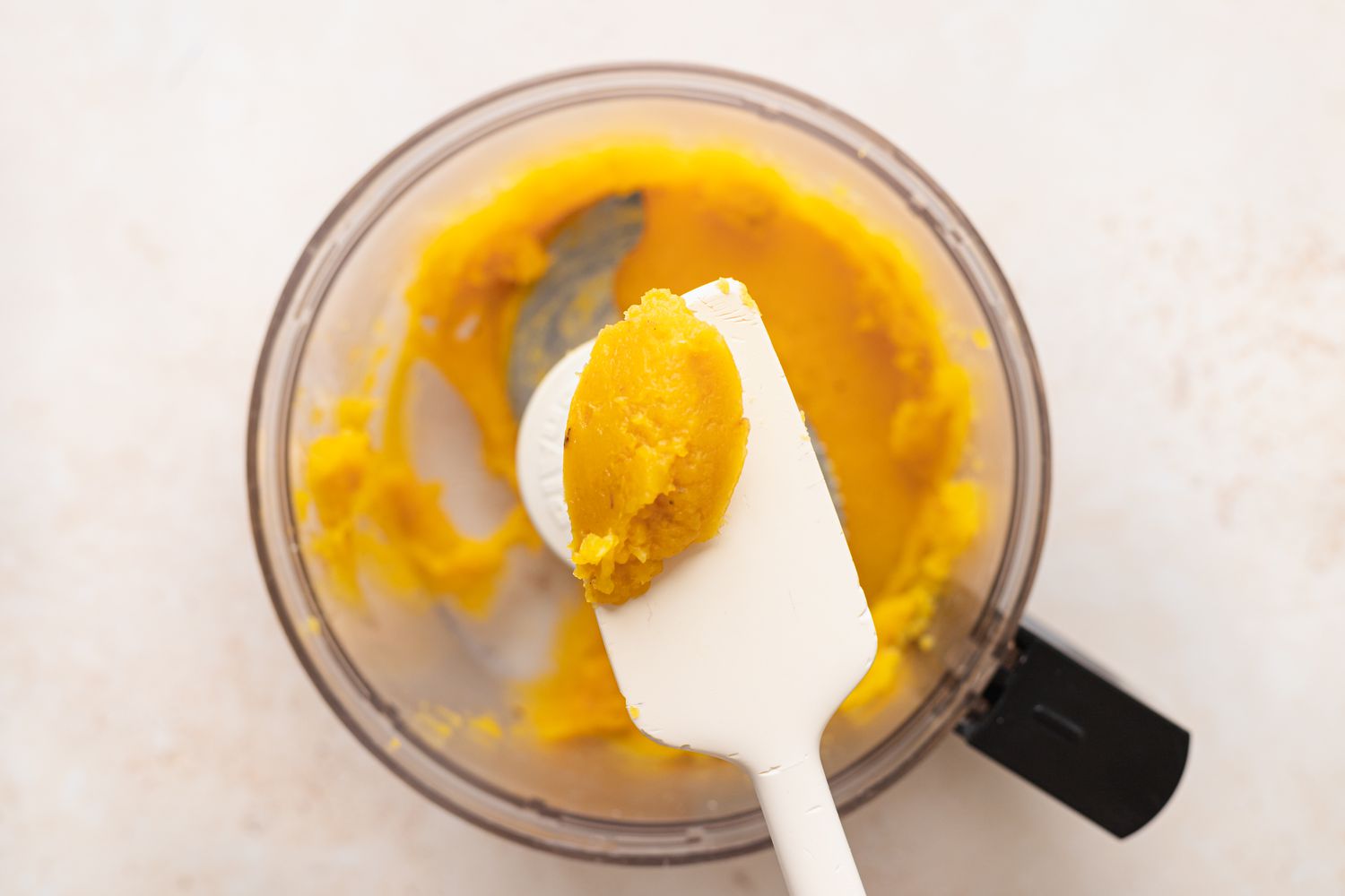 Scooping pureed squash out of a food processor to make a stuffed squash recipe.