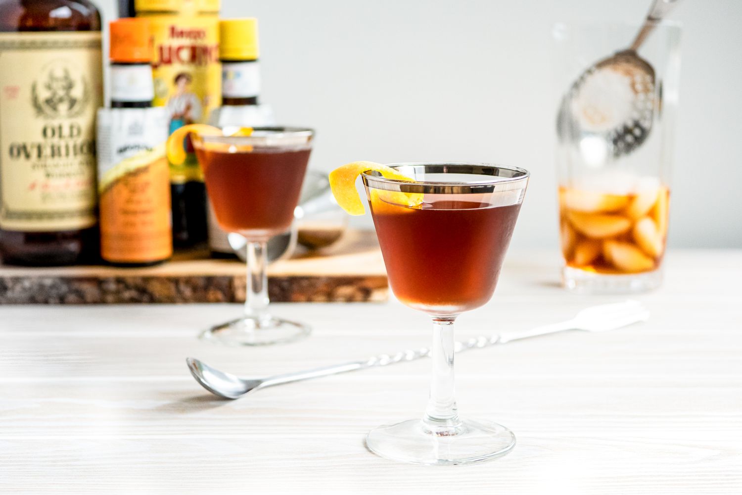 Black Manhattan with an Orange Peel and in the Background, Another Glass and Ingredients for the Cocktail