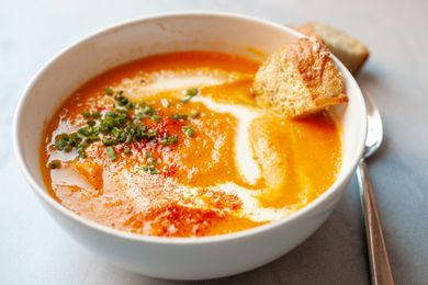 A bowl of carrot soup garnished with herbs and cream accompanied by a piece of bread