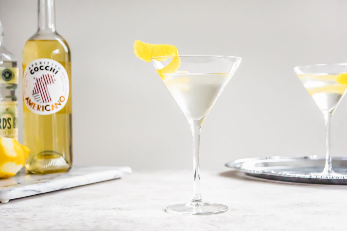 Vesper Cocktail on the Counter and in the Background, on the Left, a Marble Tray with Americano and Gin Bottles and on the Right, Another Glass on a Silver Tray