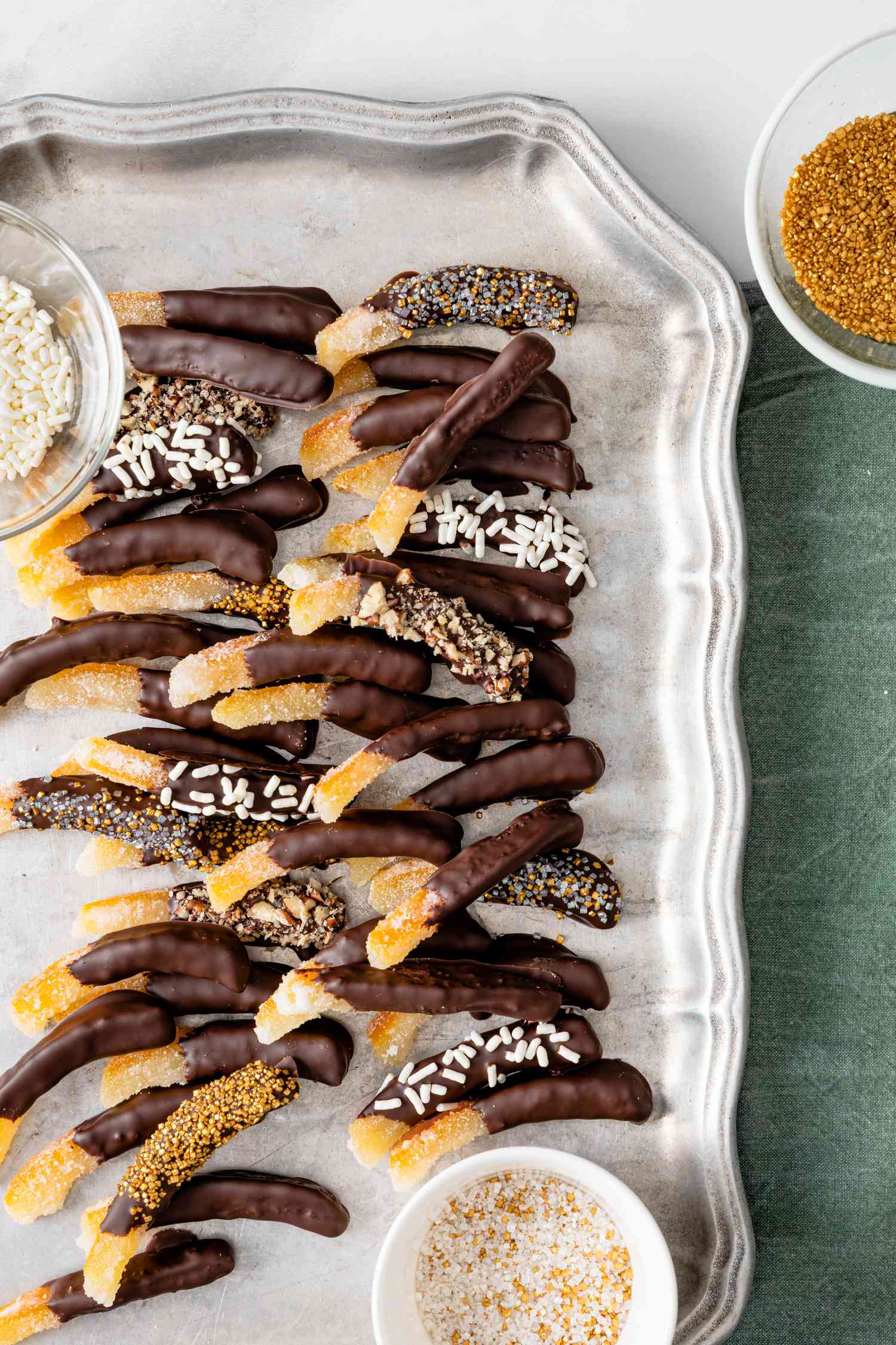 Chocolate Covered Orange PeelsChocolate Covered Orange Peels on a Tray with Two Bowls of Toppings. Some Chocolate Covered Orange Peels Are Topped with Sprinkles and Nuts.