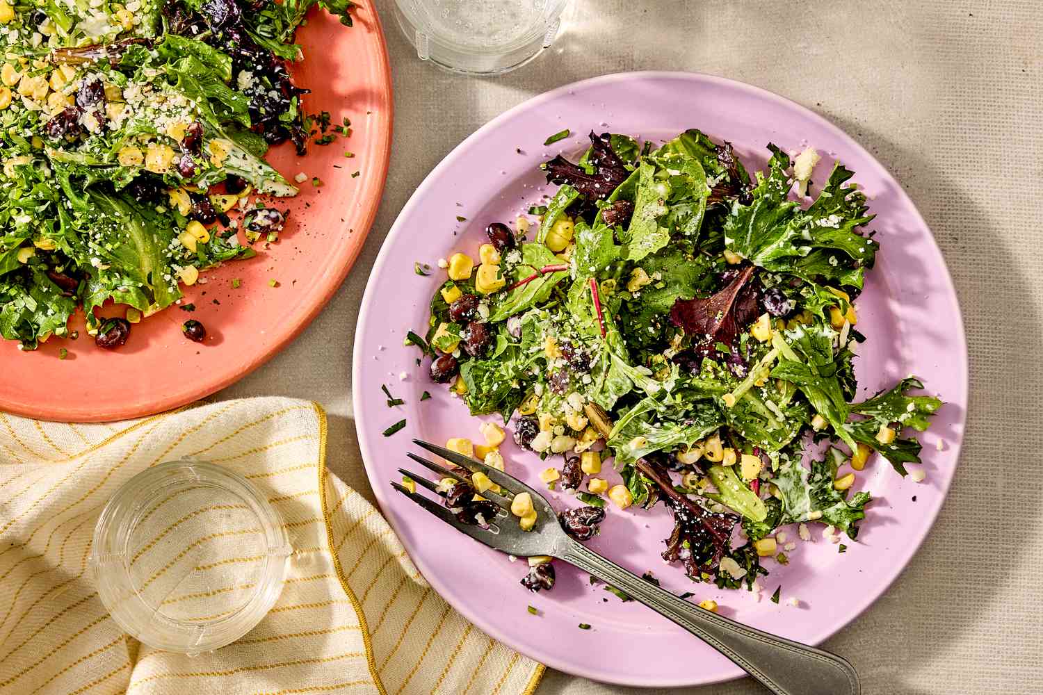 Two plates of salad with mixed greens, corn, and black beans, a fork on one plate
