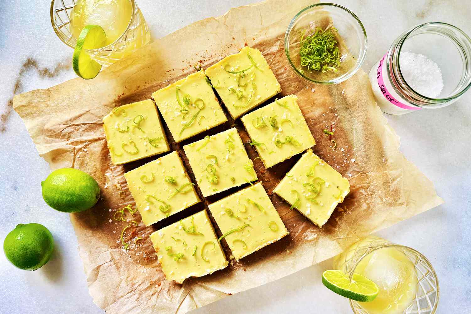 Nine cut squares of dessert with lime slices nearby prepared on parchment paper