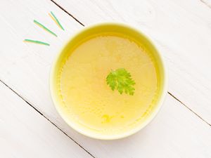 A bowl of chicken broth with a leaf garnish on a wooden surface
